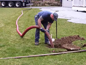 Septic pumping technician servicing a residential septic tank with a vacuum hose in Champaign, IL