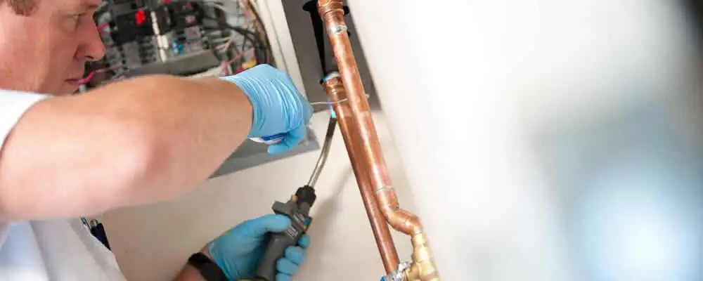 Water heater repair technician testing copper pipe connections and controls in Champaign, IL